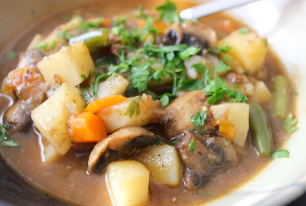 A rustic bowl of old-fashioned beef stew served on a wooden table. The stew includes tender chunks of beef, vibrant orange carrots, golden potatoes, a